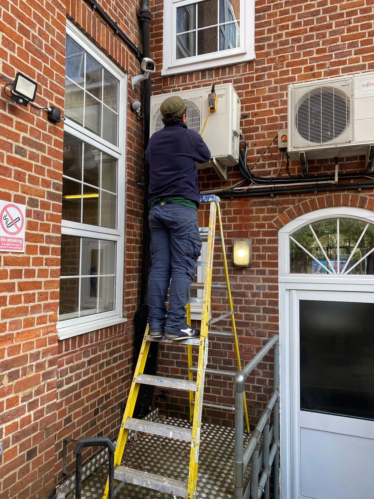 Engineer servicing a Mitsubishi outdoor AC unit on a London brick building